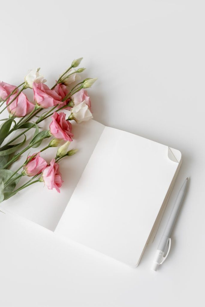 Open notebook with pink and white flowers and a pen. Perfect for minimalistic designs.